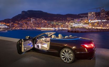 Black sports car with driver's door open, parked beside a harbour at night