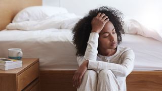 Woman sitting next to a bed with her face in her hand