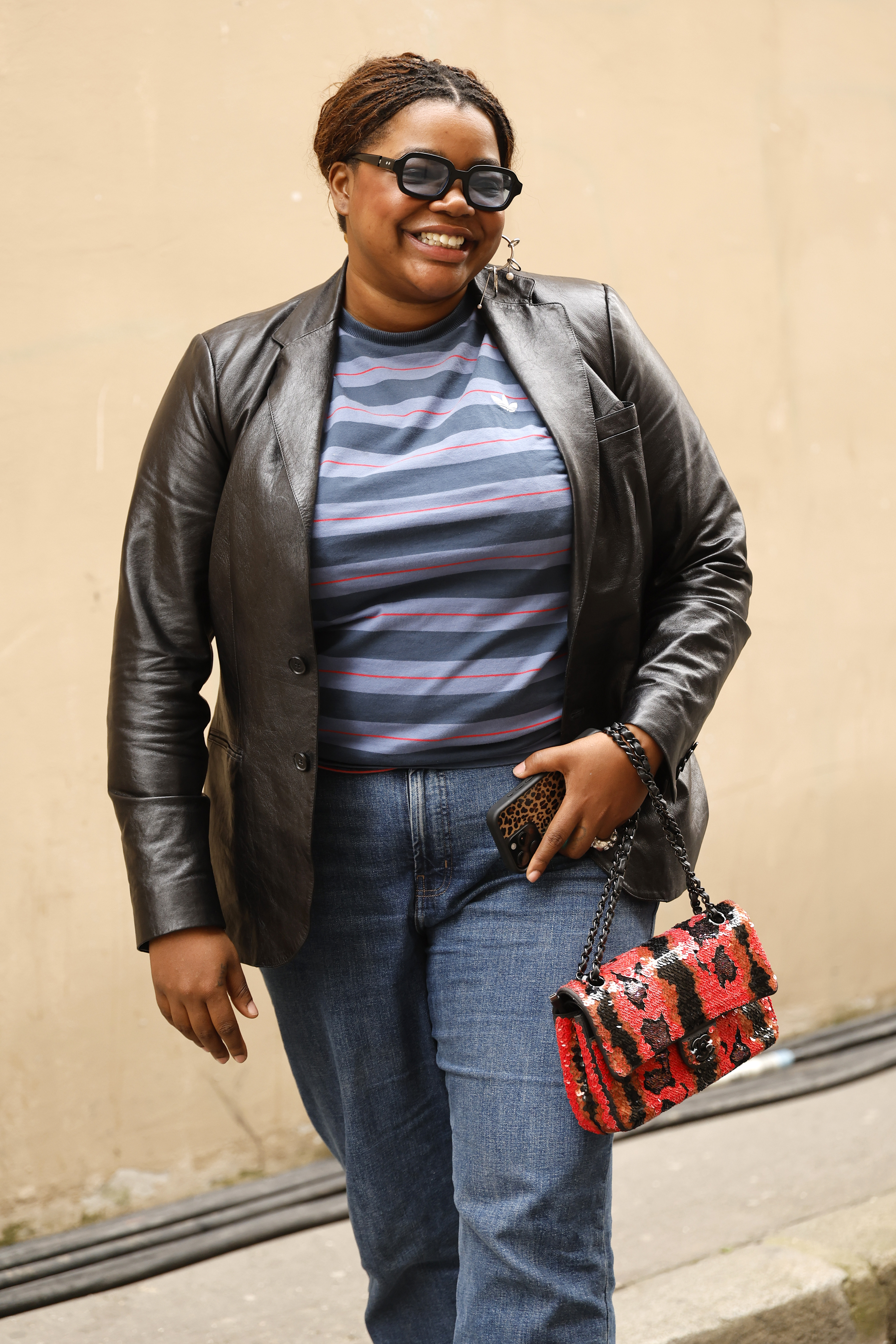 PARIS, FRANCE - MARCH 07: Gabriella Karefa-Johnson wears blue and red Adidas striped t-shirt, black leather jacket, medium wash jeans, red and black snake skin print bag, outside Junya Watanabe, during Day Six of Paris Fashion Week - Womenswear Fall/Winter 2026/2027 on March 07, 2026 in Paris, France. (Photo by Claudio Lavenia/Getty Images)