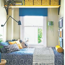 A narrow bedroom painted in a soft yellow paint shade with a yellow wall shelf above the window