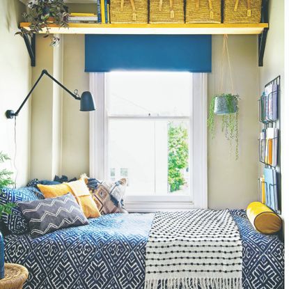 A narrow bedroom painted in a soft yellow paint shade with a yellow wall shelf above the window