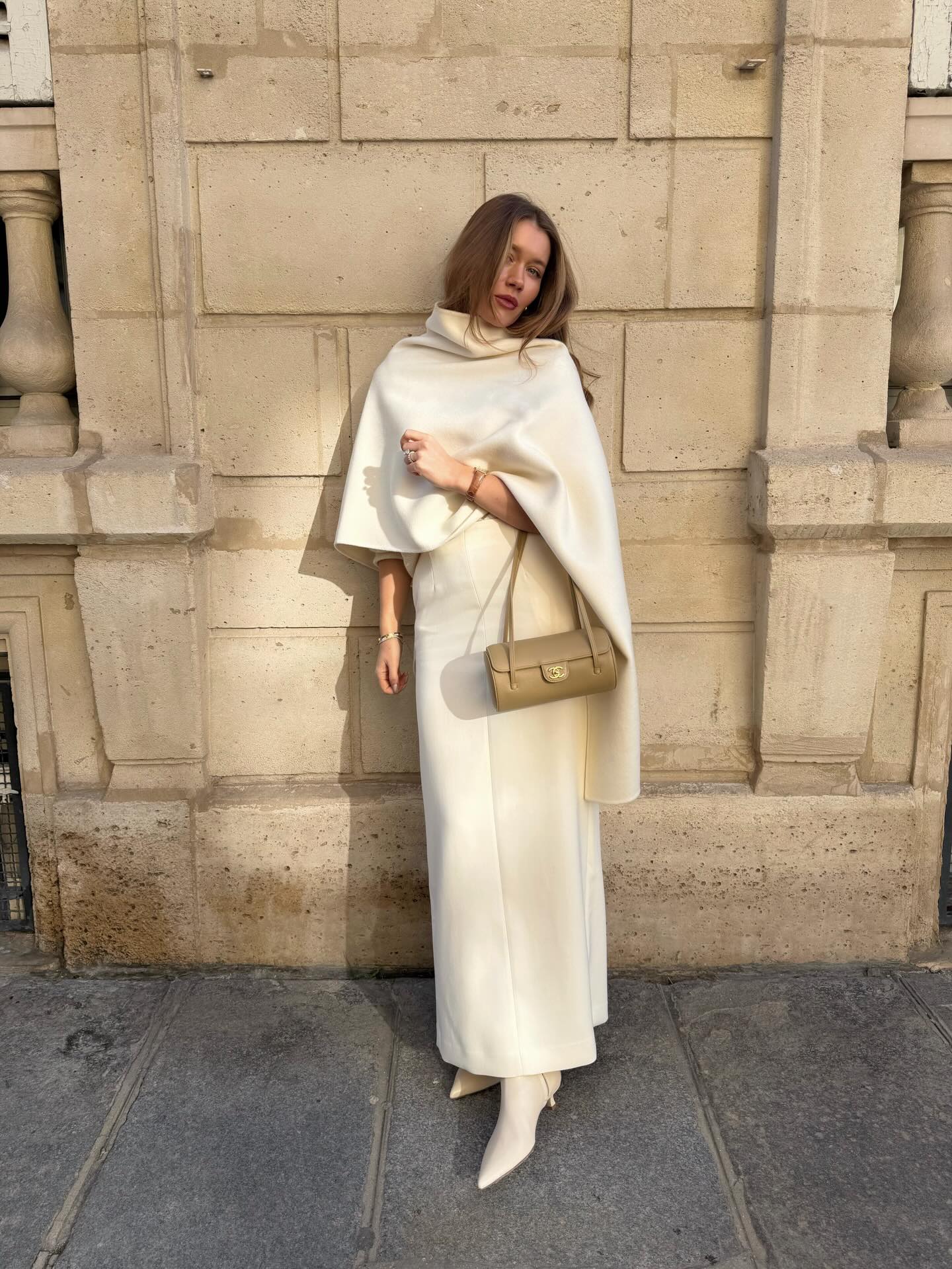 An image of an influencer in Paris wearing a cream-coloured cape, maxi skirt and kitten heels boots holding a beige baguette handbag