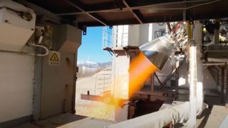 closeup image of a rocket engine firing, producing a streak of orange flame during a ground-based test