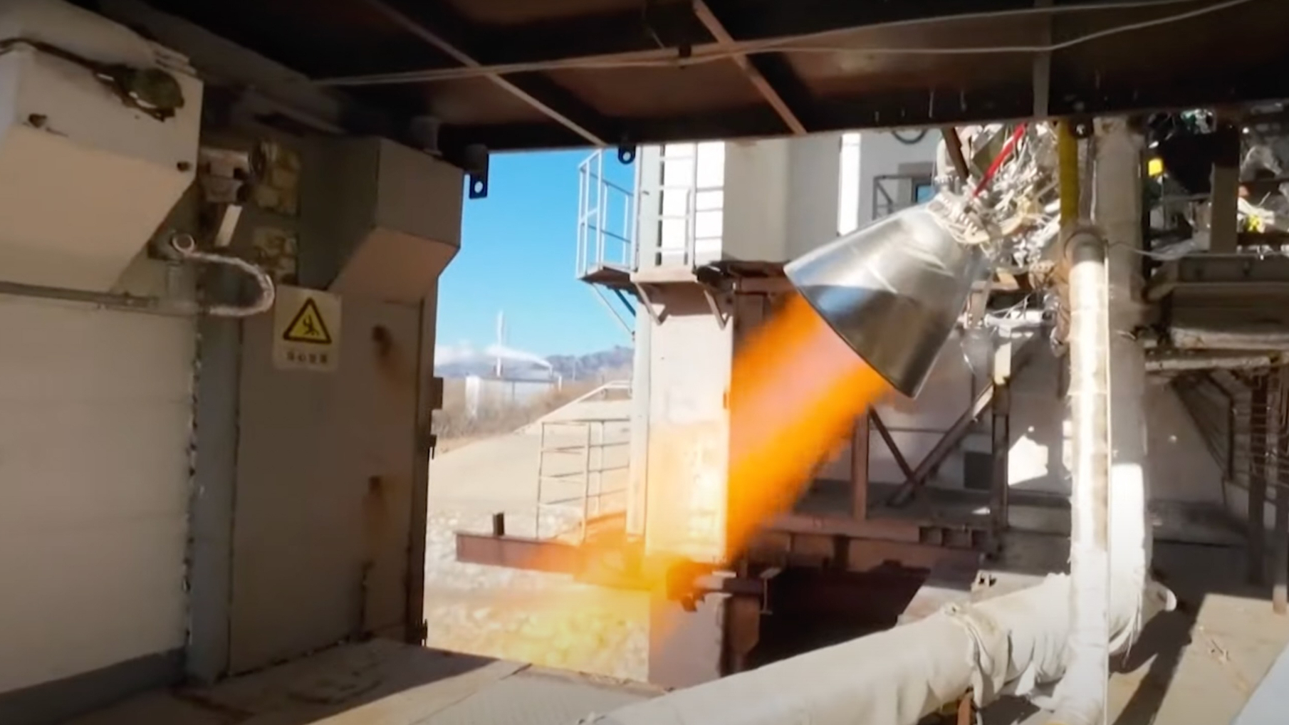 closeup image of a rocket engine firing, producing a streak of orange flame during a ground-based test