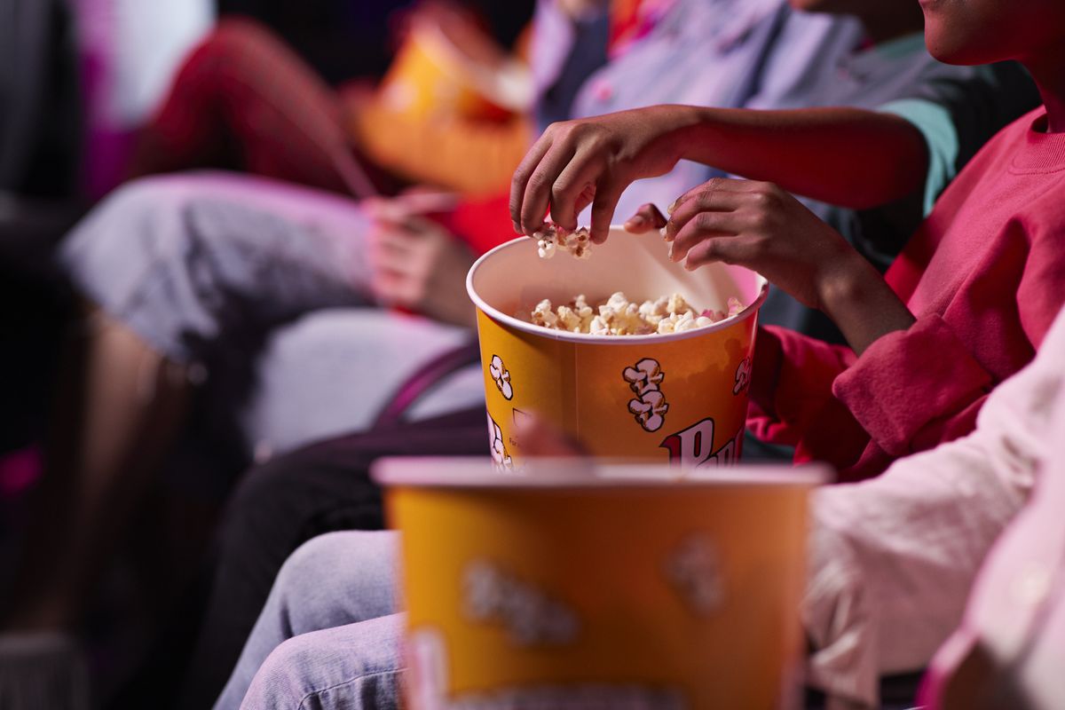 Midsection of friends sharing popcorn in theater