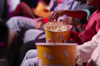 Midsection of friends sharing popcorn in theater