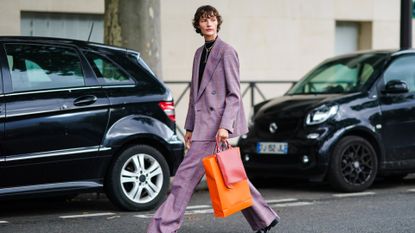A model wears a black turtleneck pullover, a necklace, a purple checked oversized blazer jacket, a red leather bag, flared suit pants, black leather pointy shoes, outside Hermes, during Paris Fashion Week - Womenswear Spring Summer 2021 on October 03, 2020 in Paris, France.