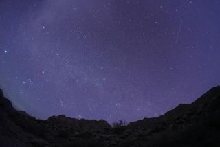 a meteor streaks through a starry sky above mountains