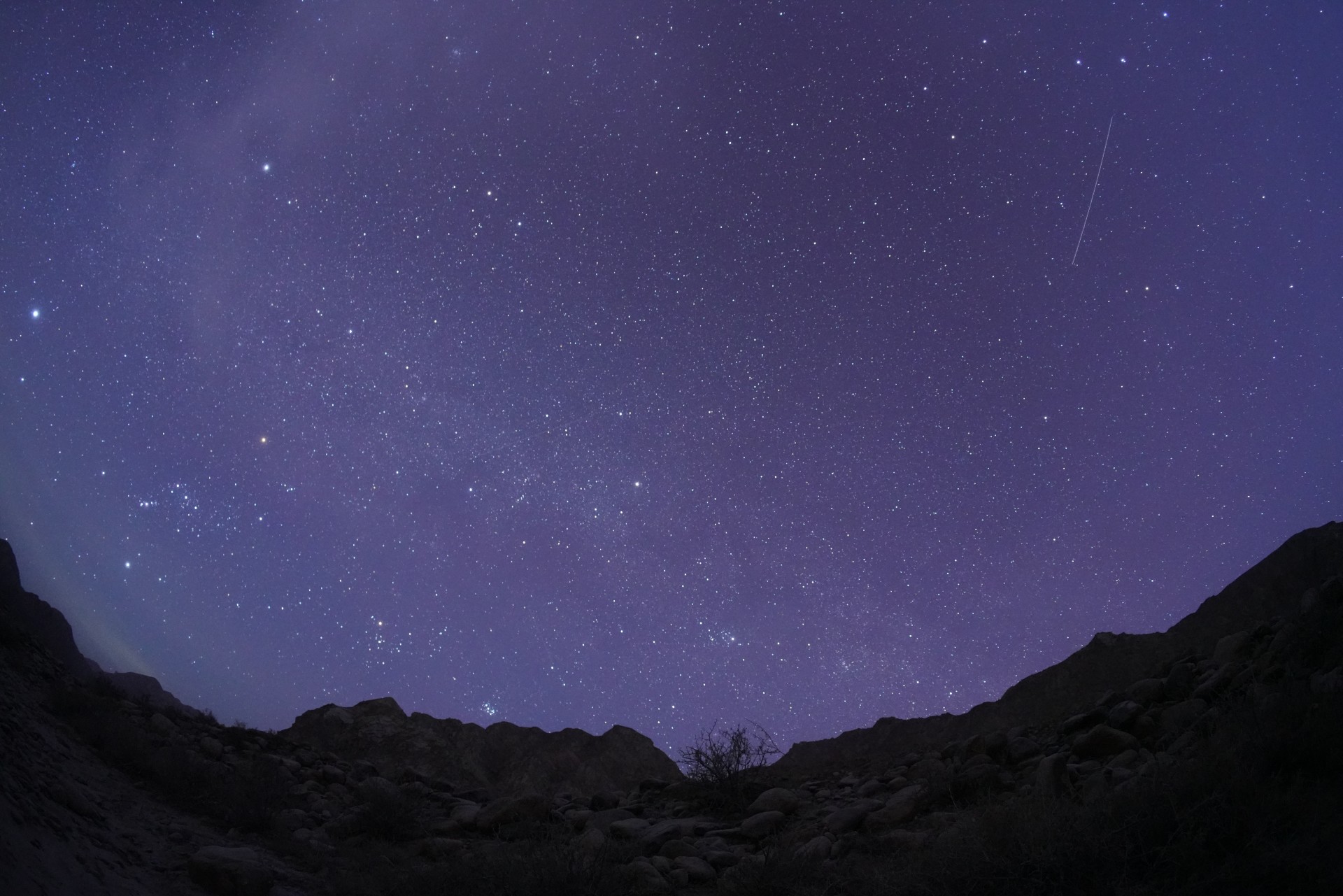 A meteor streaks through a starry sky over mountains