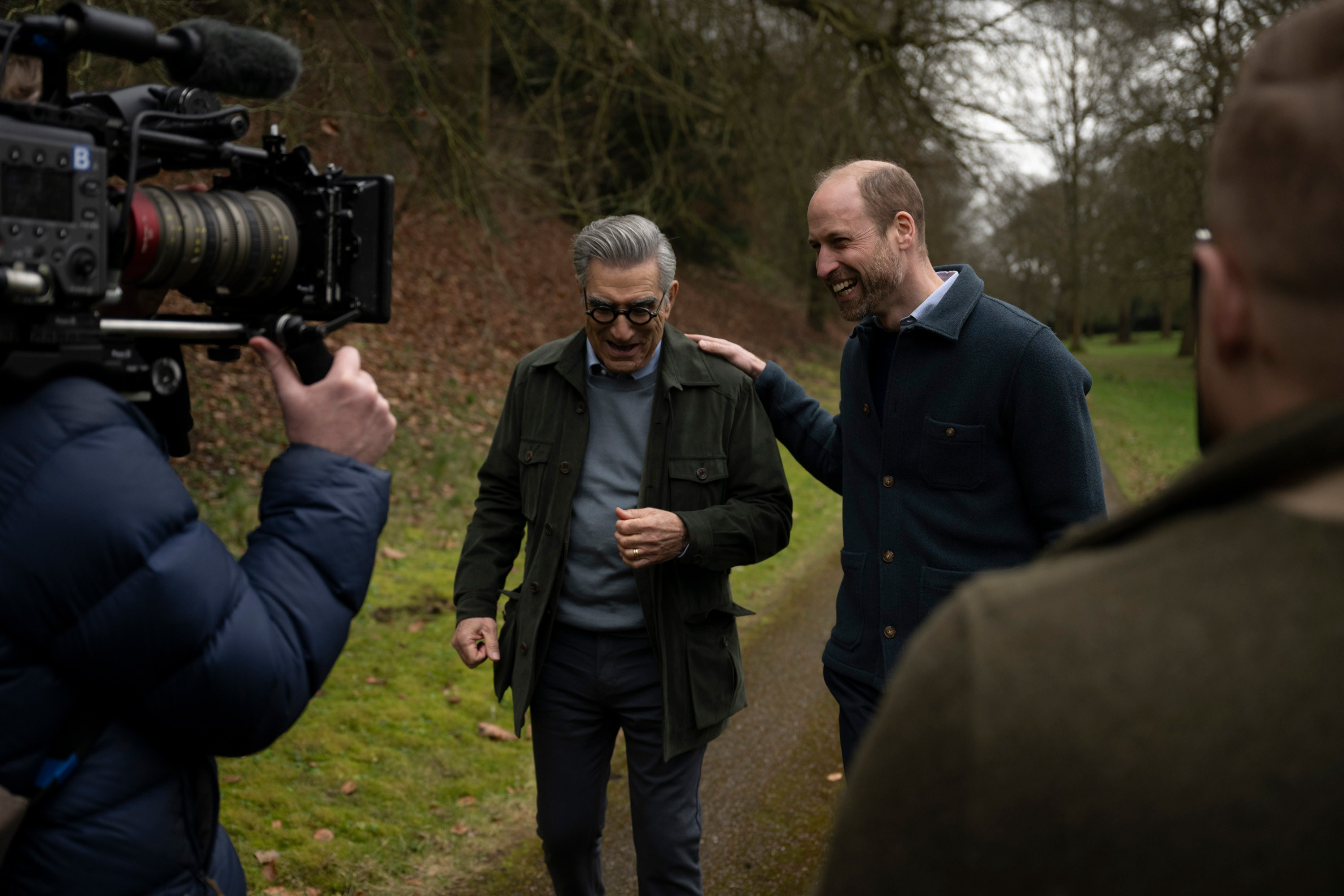 Prince William putting his hand on Eugene Levy&#039;s shoulder walking in the park while a cameraman films him