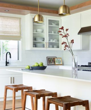 A white tiled kitchen with woven wooden stools at a large island