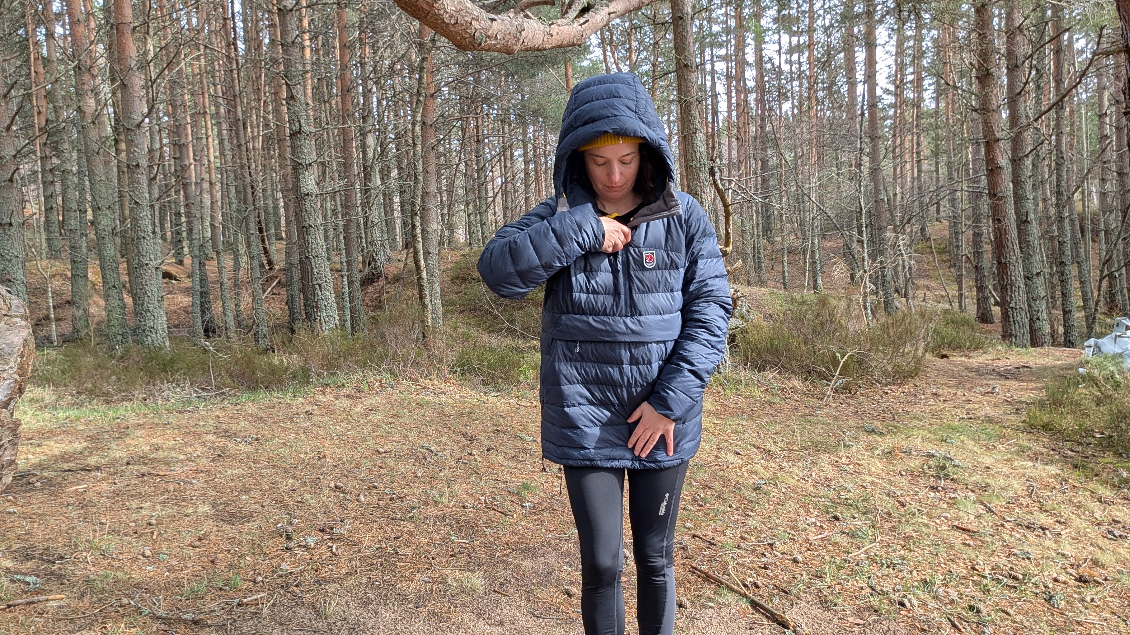 A woman in a forest zipping up a blue down jacket