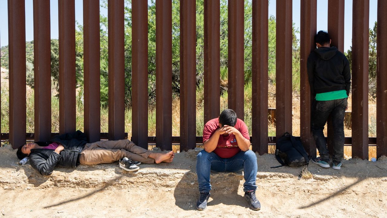 Migrants rest at the iron border fence as they wait to be processed by the US Border Patrol agents near Jacumba Hot Springs, California