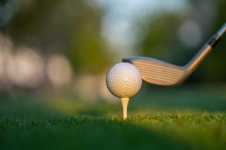 Golf ball on green grass ready to be struck on golf course background - stock photo