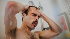 Man in shower with eyes closed, hands on scalp and water dripping from his head