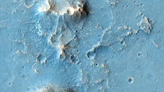 a false-color blue-and-green image of a mountainous landscape dotted with craters