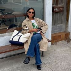 @sashamei sitting wearing leather clogs, jeans, and a trench coat