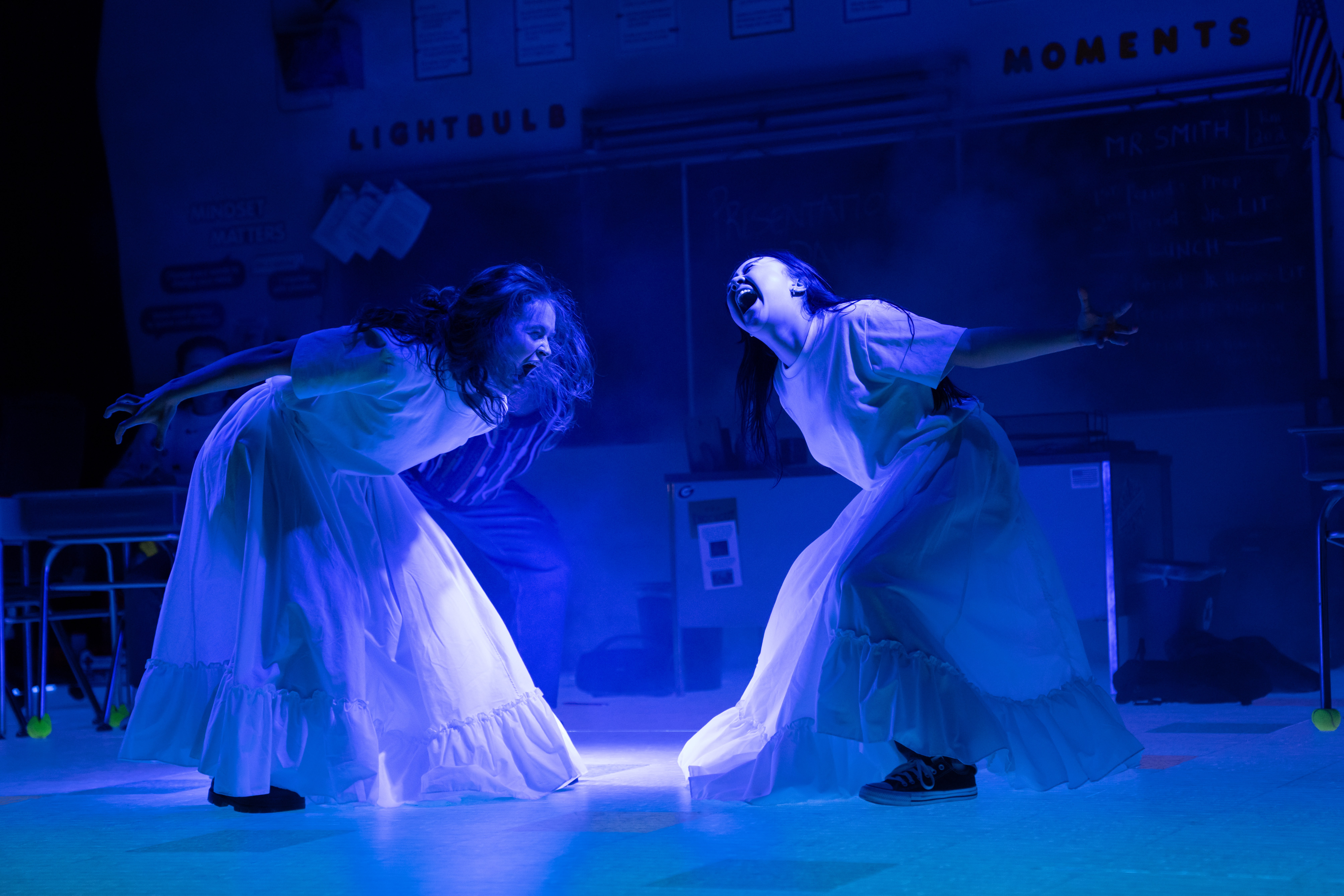 two girls including sadie sink wearing long white dresses dancing in a blue light in the play john proctor is the villain