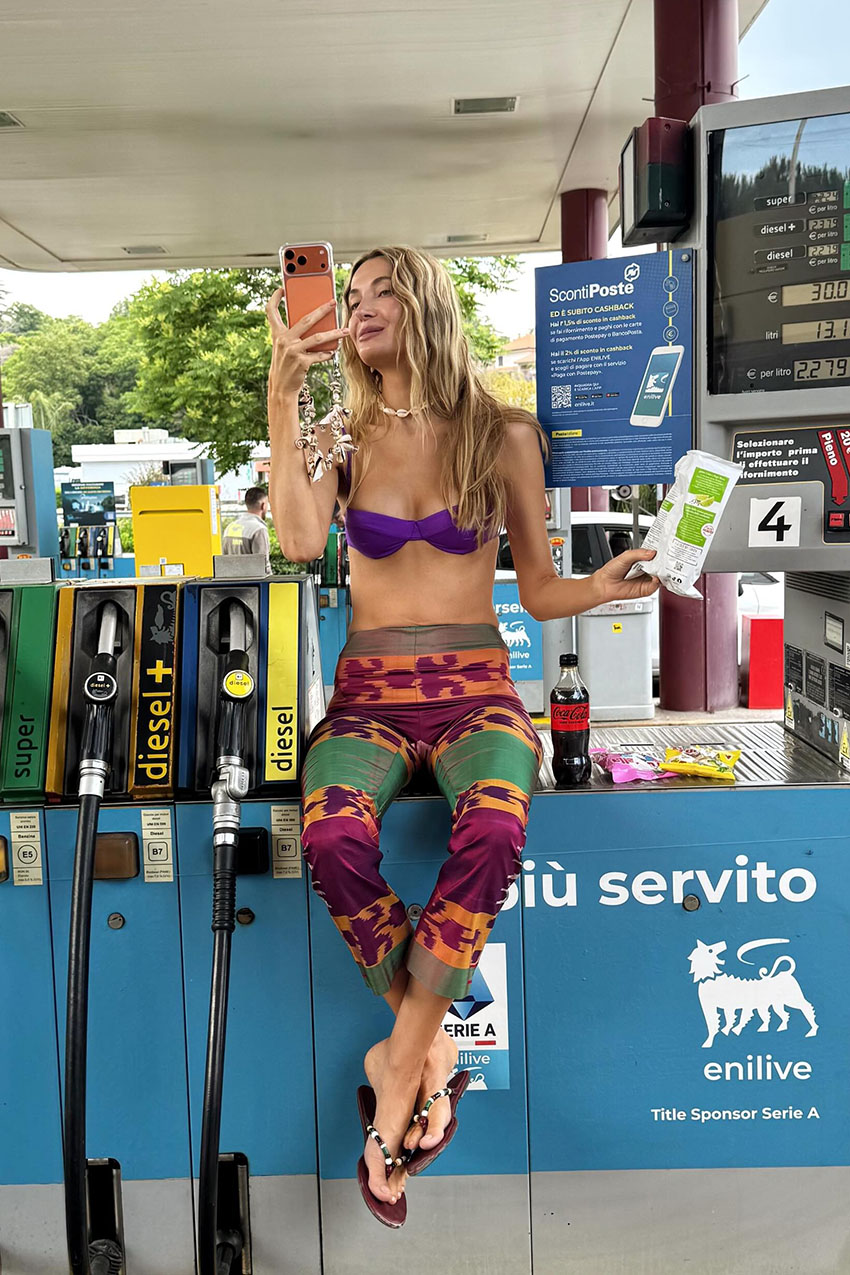 a woman wearing a purple bikini top, multicolor pants, and beaded flip-flops