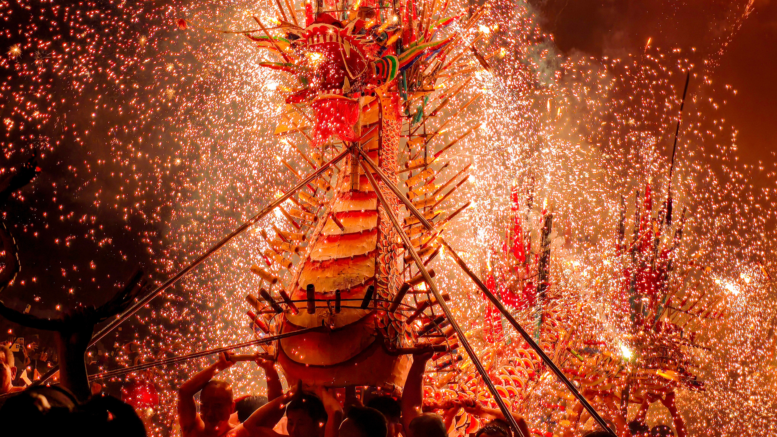 A vibrant dragon dance at a festival, surrounded by a shower of golden sparks from fireworks, people carry the dragon