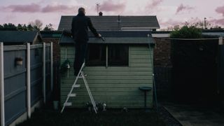 Man on ladder working on shed roof