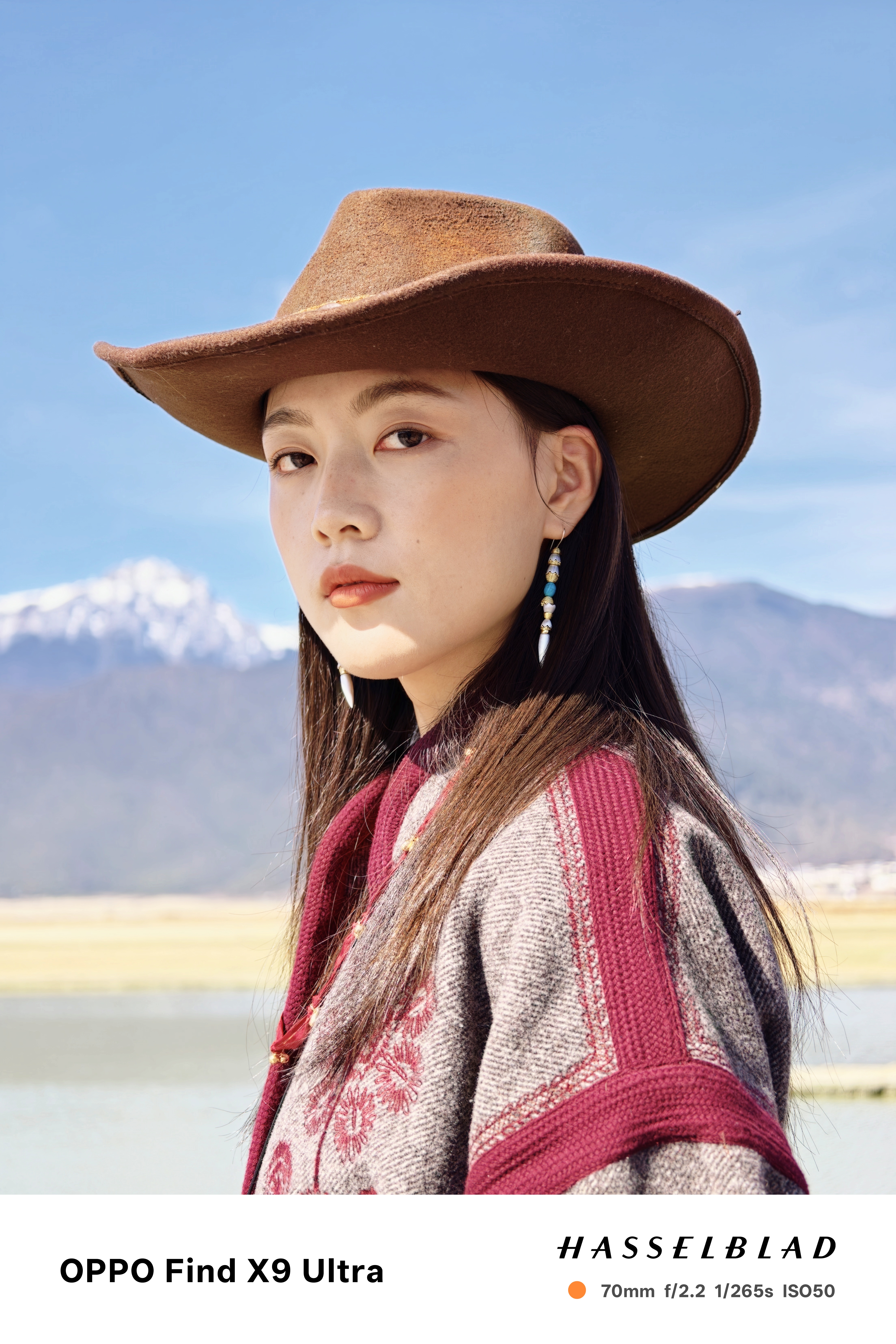 Chinese woman in a cowboy hat posing for a photo with a snoy mountain backdrop