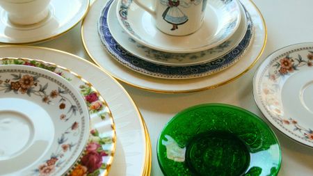 Close-up of random mismatched porcelain china plates saucers dishes decluttering table organization background estate backdrop.