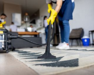 Close-up on a professional cleaner vacuuming a carpet while working at an apartment