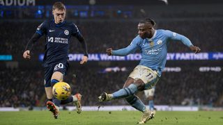 Cole Palmer (L), in navy blue kit, attempts to block a ball in from Jeremy Doku, in sky blue shirt and white shorts, at the Man City vs Chelsea live stream.