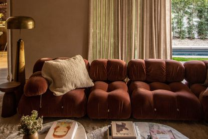 a rust sofa with beige sheer curtains behind