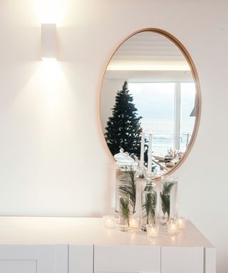 A table with Christmas lights with a mirror above it reflecting a Christmas tree