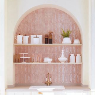 Arched recess in a kitchen tiled in textured pink tiles with open shelves