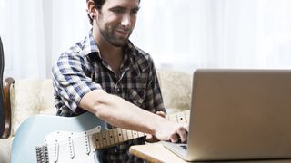 Man with blue guitar sits in front of a laptop