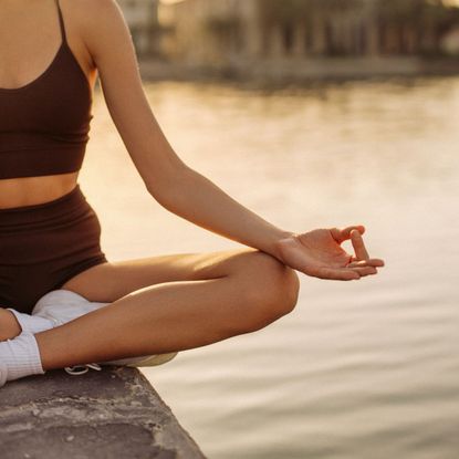 A woman practicing yoga by the river, crossed legged and hands in prayer