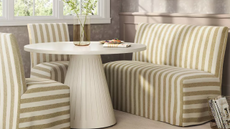 Striped dining banquette and chairs clustered around a round dining table in a sunlit breakfast nook overlooking a window