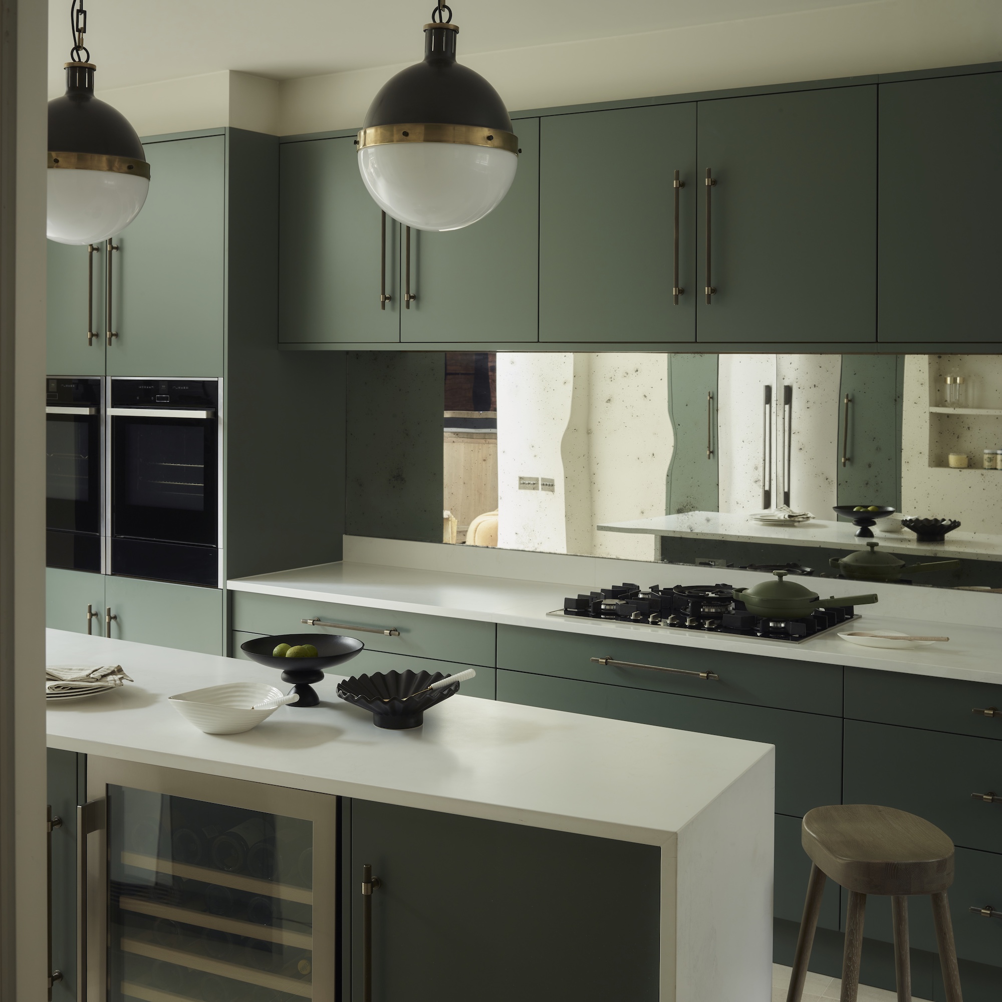 kitchen with green cabinets, mirrored splashback and white island unit with globe pendant lights above