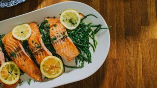 Fillets of salmon sitting on serving plate with green vegetables and round slices of lemon, representing one of the foods for seasonal affective disorder