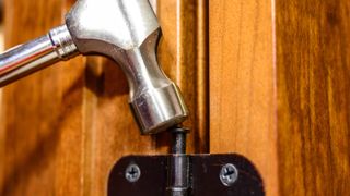 A hammer knocking a pin back into a door hinge