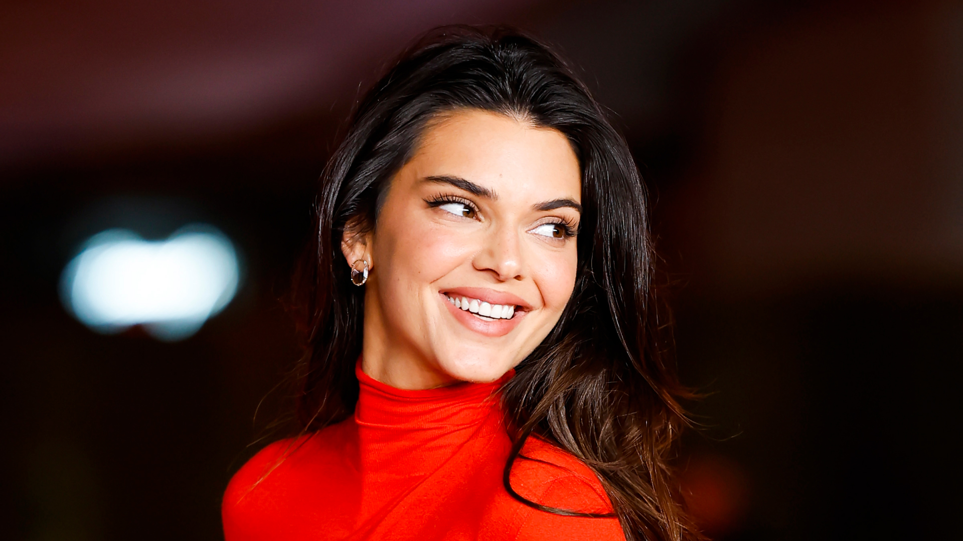 Kendall Jenner has long dark brown hair and wears a bright red turtle neck dress