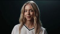 Sydney Sweeney smiling into the camera wearing a white football jersey in Novig ad