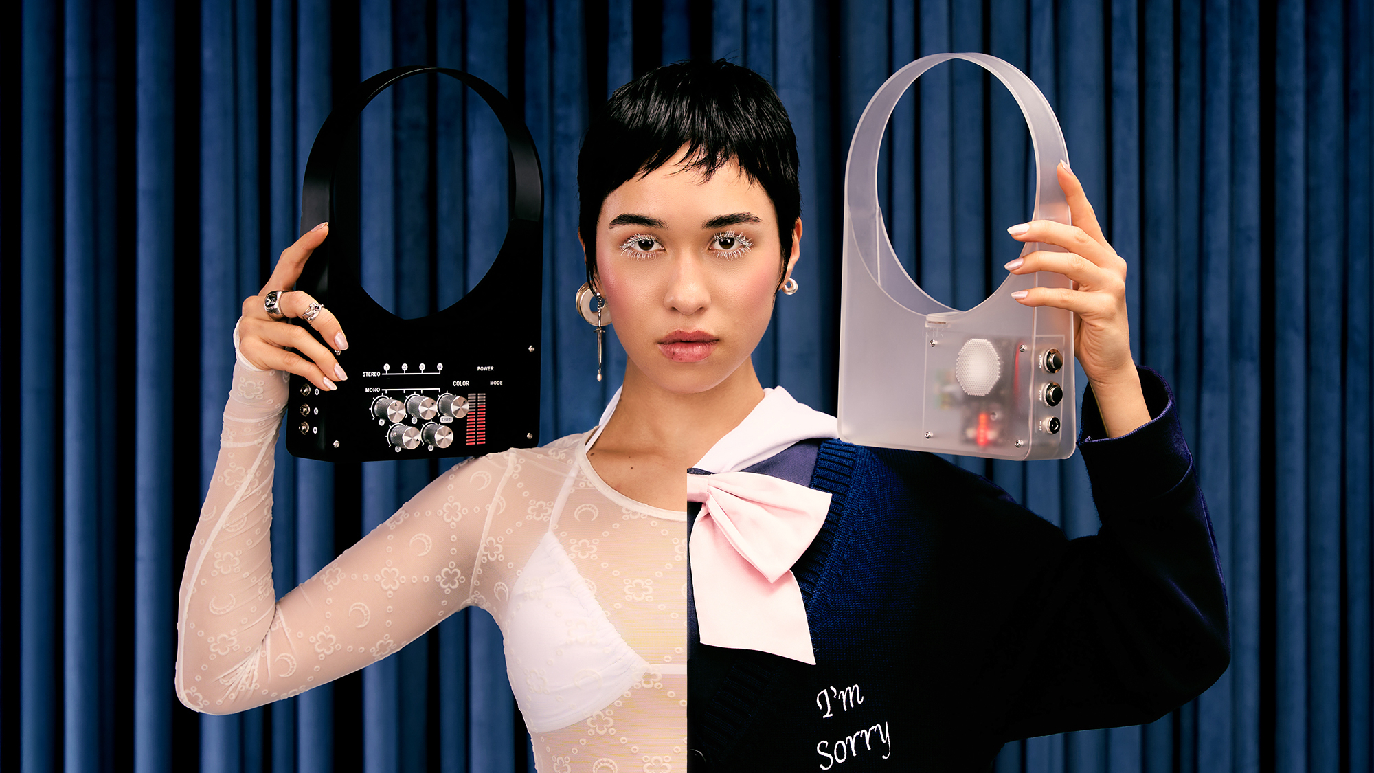 A woman holding a Nik Bentel speaker bag and a mixer bag, almost like earrings, wearing a half-and-half monochrome dress, in front of a navy curtain