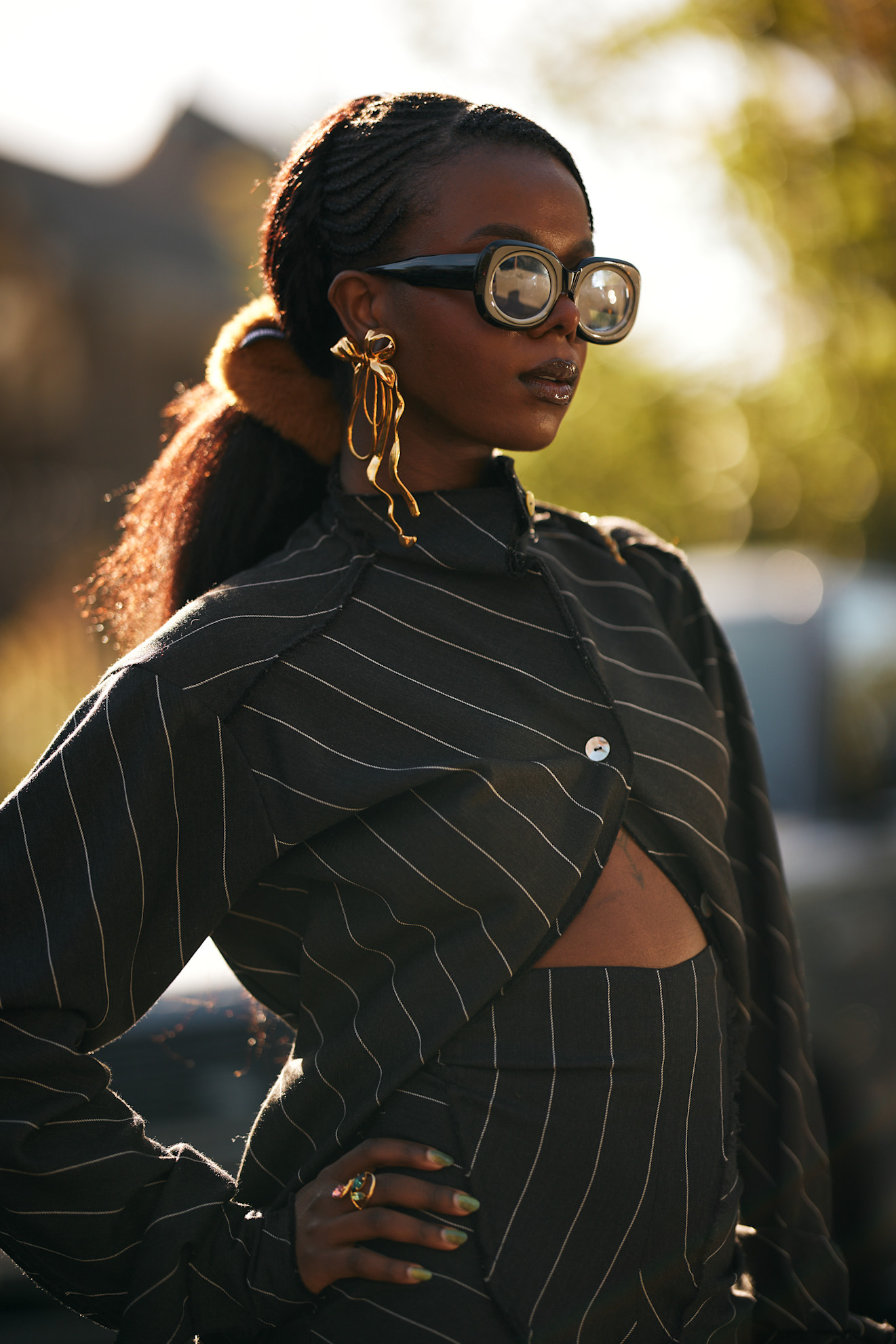 girl in a striped outfit with gold bow earrings, sunglasses, and a ponytail