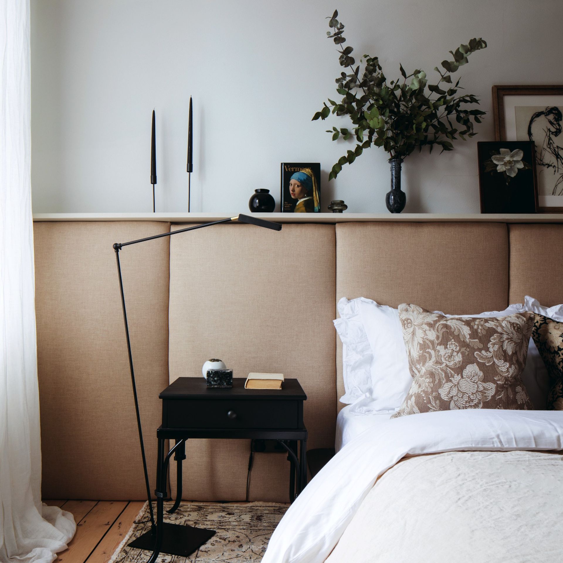 Cushioned panelled bedroom wall, bed with white and neutral bedding, bedside table