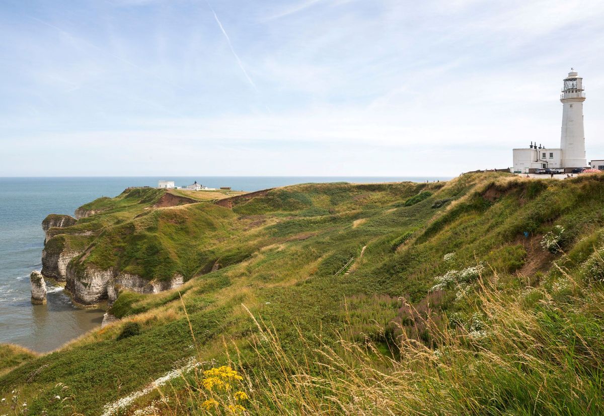 The coastal site of the build with grass covered headland and a lighthouse