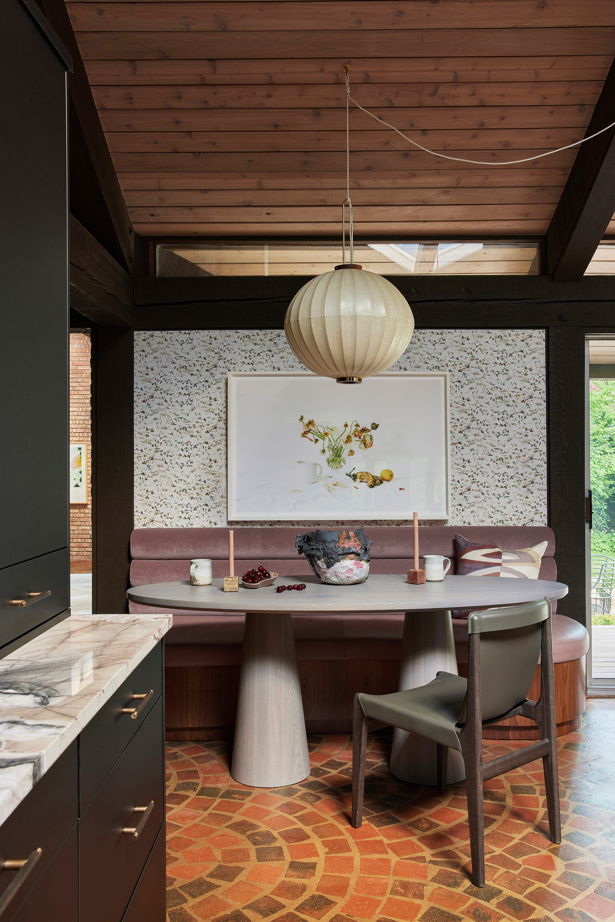 Grey breakfast with dark wood and olive chair, lilac banquette seating, brick floor and cream pendant light