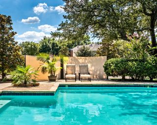 Large backyard swimming pool flanked with paving slabs and two sun loungers