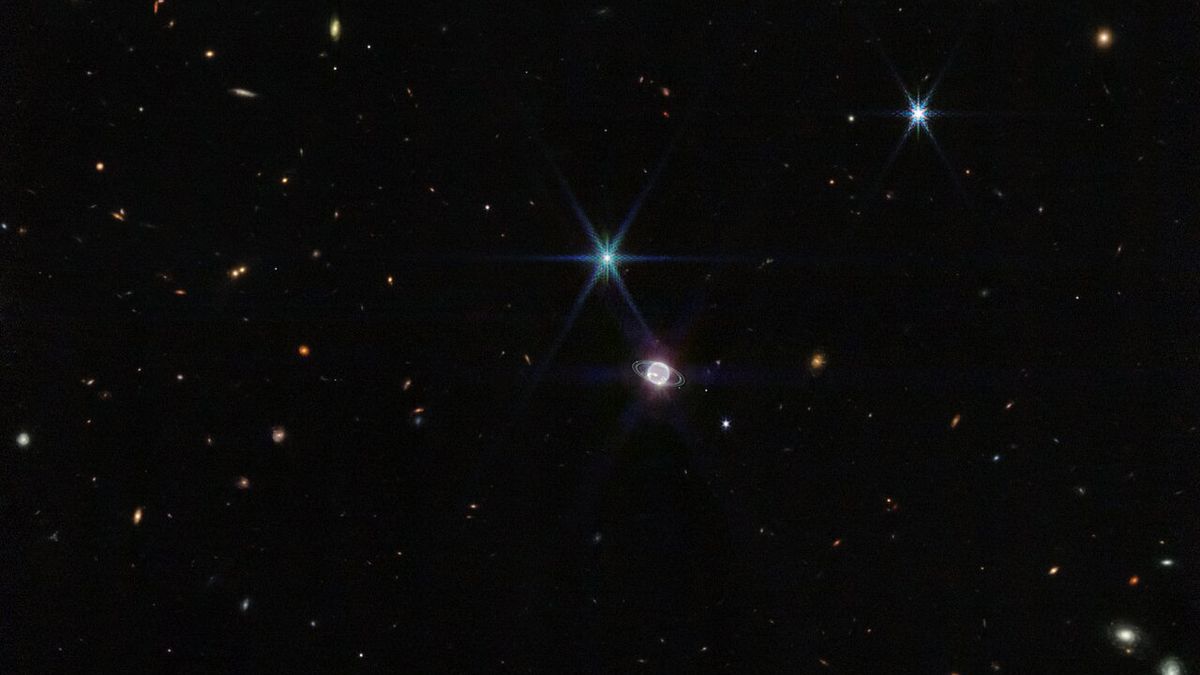 The solar system's most distant planet Neptune captured by the James Webb Space Telescope on the backdrop of a galaxy-studded sky.