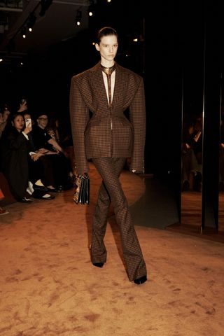 a model walks the shiaparelli runway with a nipped in waist and exaggeratedly skinny trousers