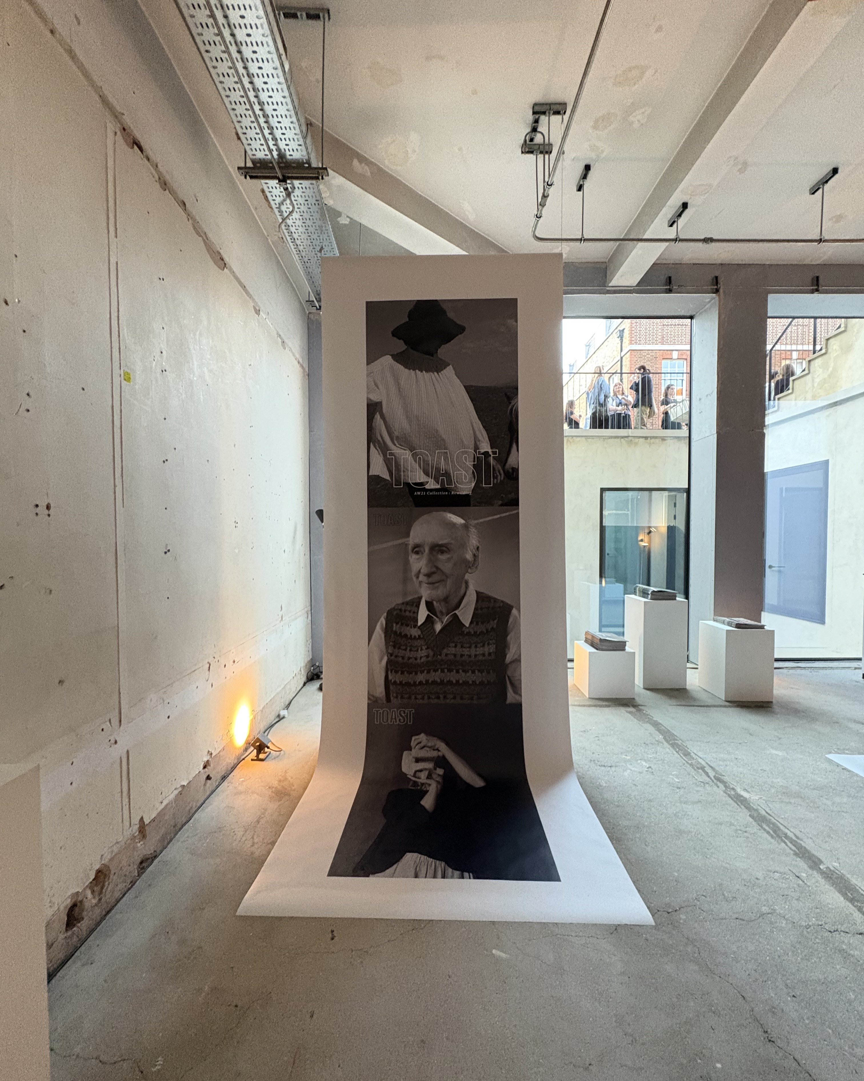 Installation view of a fashion and design exhibition featuring clothes, homeware, retro-looking tvs showcasing audiovisual works, large posters, and more.