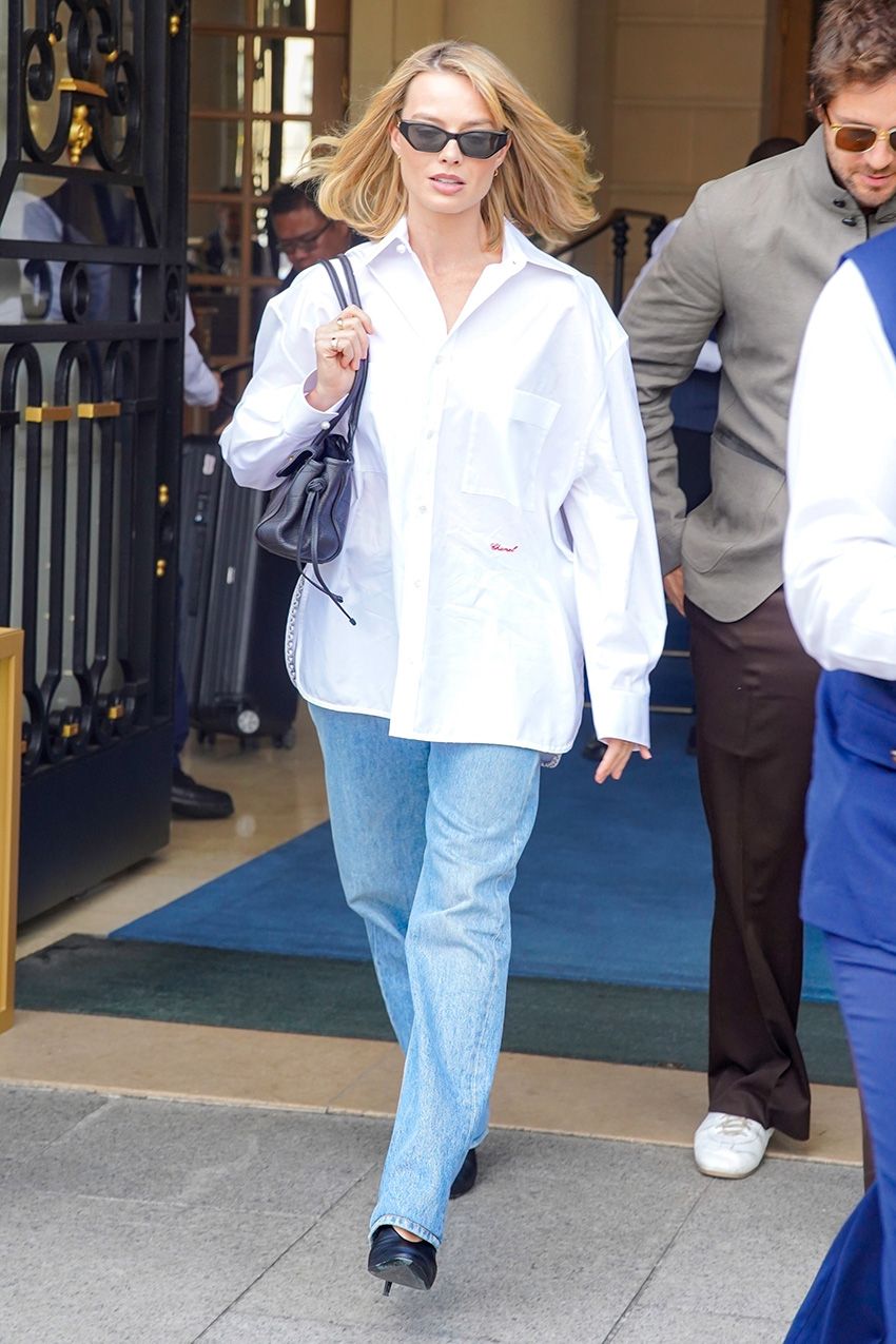 Margot Robbie wearing a white button-down, light-wash jeans, and black pumps, leaving The Ritz in Paris with husband Tom Ackerley
